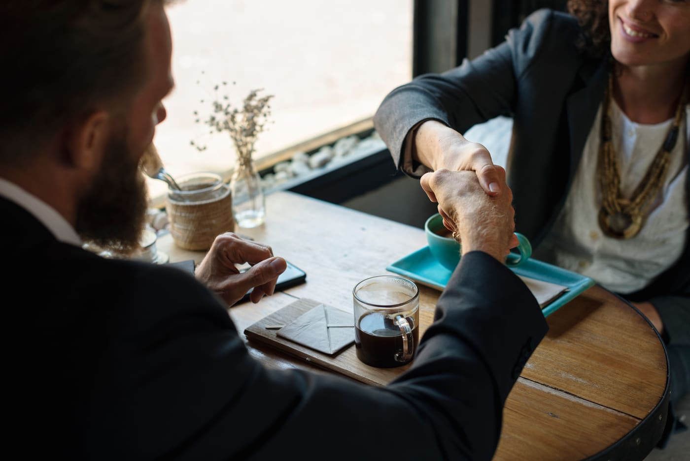 Two business people shaking hands across a café table